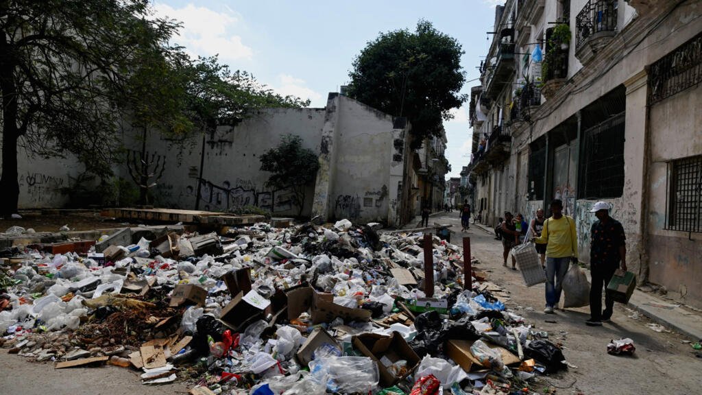 Peatones caminan cerca de una pila de basura acumulada en las calles de La Habana por los problemas de combustible que demoran la recolección. 15 de febrero de 2026.