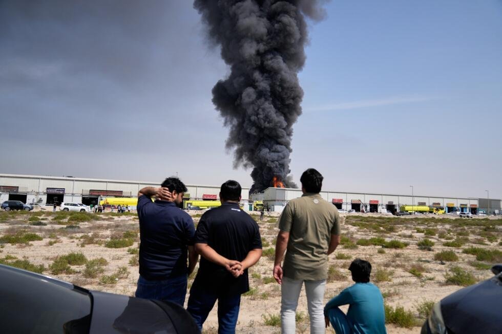 Residentes observan cómo las llamas y una columna negra de humo se elevan desde un almacén en la zona industrial de la ciudad de Sharjah, en los Emiratos Árabes Unidos, tras los informes de ataques iraníes en Dubái. 1 de marzo de 2026.