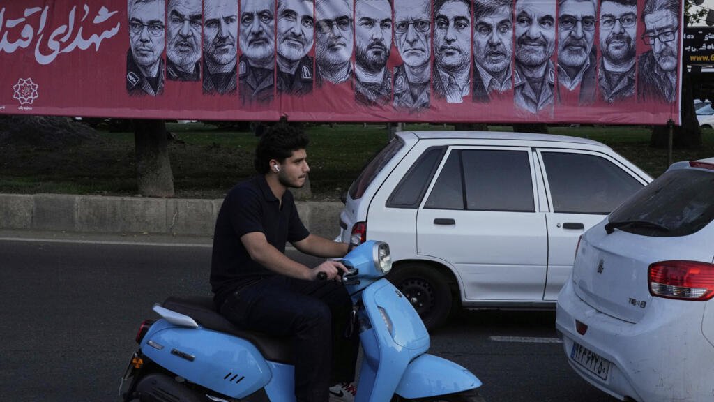Vehículos circulan frente a una pancarta con retratos de los comandantes de las fuerzas armadas iraníes y científicos nucleares que murieron en un ataque israelí, en la plaza Tajrish, al norte de Teherán, Irán, el lunes 30 de junio de 2025.