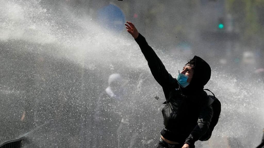 Un joven lanza piedras a la policía, que dispara un cañón de agua en una protesta estudiantil contra la propuesta del gobierno de reducir el presupuesto educativo y contra el aumento de los precios de la gasolina en Santiago de Chile, jueves 26 de marzo de 2026. (