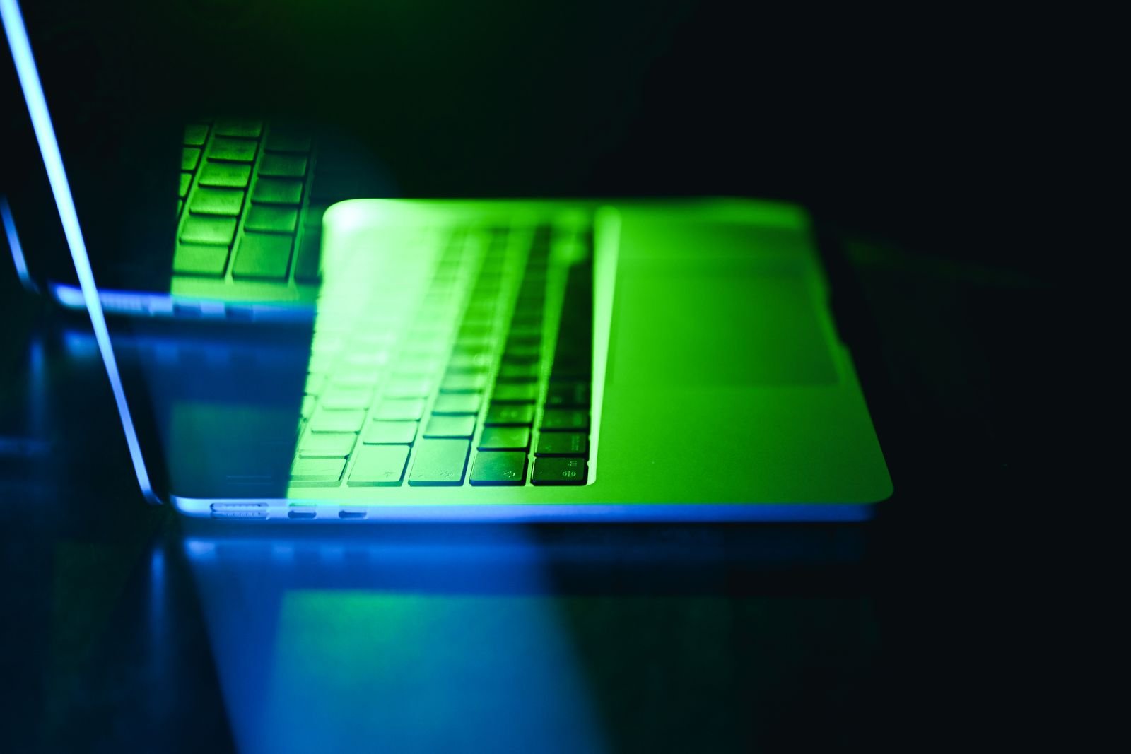 El teclado de un ordenador porttil brilla con una luz verde y azul que se refleja en una superficie oscura