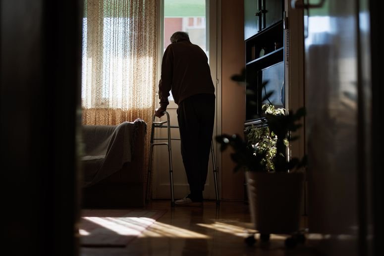 Un hombre adulto mayor mirando por la ventana, sostenido de una andadera.