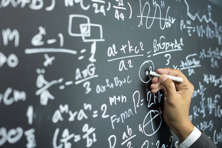 una mano escribe en un pizarrón; preguntas sobre el universo