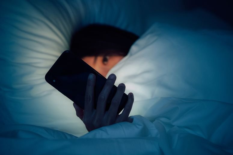 Mujer escondida bajo la manta, charlando y navegando por internet con su smartphone a altas horas de la noche en la cama. 
