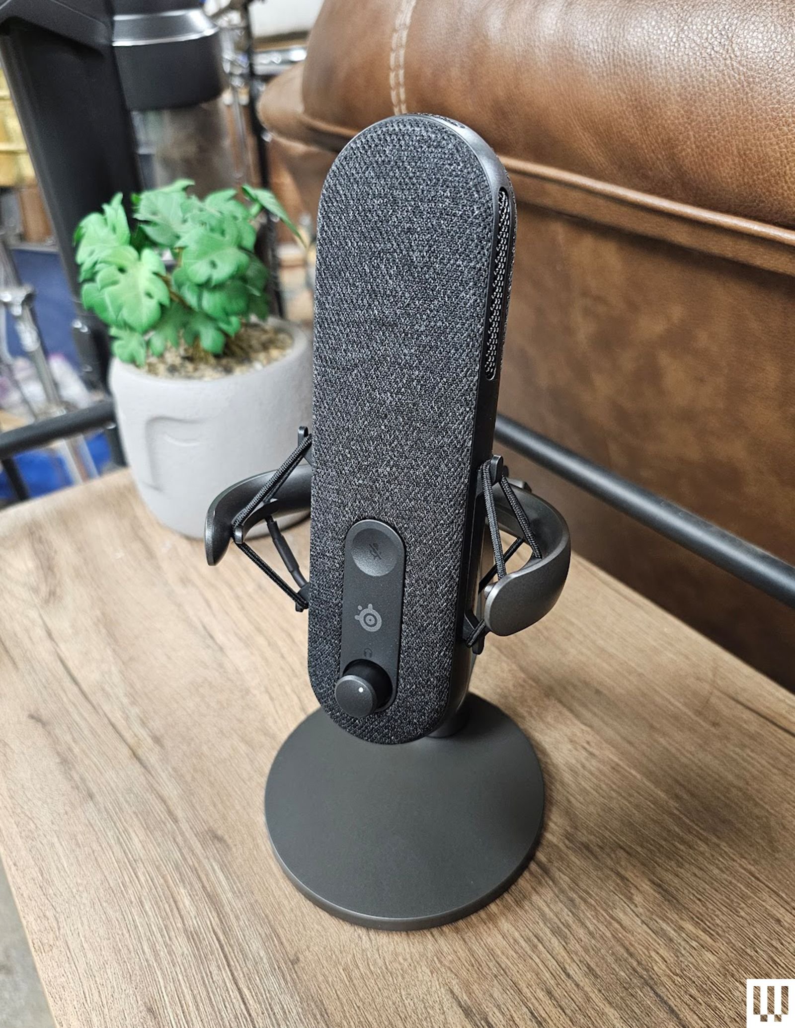 El micrófono SteelSeries Alias de forma ovalada sobre un soporte circular con una cubierta de malla en la parte frontal...