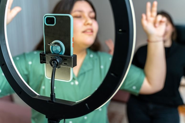 Adolescente grabando un video con su teléfono en un aro de luz. 